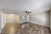 This single-floor home offers a practical and well-designed layout across two bedrooms and two bathrooms. The living room serves as the welcoming centerpiece of the home, featuring rich wood-look flooring, crown molding, a textured ceiling, and a ceiling fan that enhances air circulation and ambiance. Large windows with blinds allow natural light to fill the space, creating a bright and airy atmosphere. The kitchen is efficiently designed with white cabinetry, speckled stone countertops, black appliances including a refrigerator and dishwasher, and wood-look flooring that ties seamlessly into the main living area. A pendant light fixture adds a finishing touch to the kitchen's clean aesthetic. Both bedrooms are carpeted for comfort and feature neutral-toned walls, windows with blinds for natural light, and closet storage. The primary bedroom offers a generous footprint, providing ample space for furnishings. Each bathroom is finished with wood-look flooring, a full tub-shower combination with white tile surround, brushed nickel fixtures, and speckled stone vanity countertops. The overall design palette of soft neutral tones and consistent flooring choices gives the home a cohesive, move-in-ready feel.