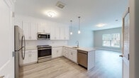 Located at 502 Howe Ave in Shelton, Connecticut, this single-floor residence offers a thoughtfully designed open-concept layout with clean, contemporary finishes. The kitchen serves as the heart of the space, showcasing crisp white shaker-style cabinetry, light granite countertops, a classic subway tile backsplash, and a full suite of stainless steel appliances including a range, over-the-range microwave, dishwasher, and refrigerator. A peninsula with pendant lighting above provides a natural division between the kitchen and the adjacent living area while keeping the floor plan open and connected. Light wood-tone luxury vinyl plank flooring runs throughout the main living areas, lending warmth and continuity to the space. The living area is bright and airy, with soft neutral wall tones and a window that frames views of the surrounding neighborhood. In-unit laundry is conveniently tucked behind louvered closet doors. The bathroom is finished with marble-look tile flooring, a modern vanity, and a full tub-shower combination. Throughout the unit, the design palette of soft greens, whites, and warm wood tones creates a calm, modern ambiance ideal for comfortable everyday living.