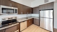 This single-floor residence offers a thoughtfully designed open-concept layout with a clean, contemporary aesthetic carried consistently throughout. Light wood-tone flooring runs seamlessly across the living areas and bedrooms, enhancing the bright, airy atmosphere created by abundant natural light from multiple windows fitted with horizontal blinds.

The kitchen is a standout feature, outfitted with rich dark-wood cabinetry extending to the upper walls for generous storage, speckled granite countertops, a white subway tile backsplash, and a full suite of stainless steel appliances including a range, microwave, dishwasher, and refrigerator. The kitchen flows directly into the open living area, which is anchored by a ceiling fan and connects to a private balcony through sliding glass doors, providing outdoor access and views of the surrounding community.

Multiple bedrooms are found throughout the unit, each featuring light wood flooring, ceiling fans, and windows that bring in natural light and exterior views. The layout provides a comfortable sense of privacy between living and sleeping areas.

The bathroom is well-appointed with light tile walls surrounding a soaking tub and shower combination, a dark-wood vanity with granite countertop, and light tile flooring. A separate water closet provides added functionality and privacy within the bathroom space.