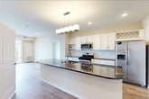 This 2-bedroom, 1-bathroom single-floor residence offers a thoughtfully designed open-concept layout that maximizes both functionality and comfort. The kitchen and living room share a seamless, open space anchored by a curved granite island with an undermount sink and modern pendant lighting. The kitchen is equipped with stainless steel appliances — including a gas range, built-in microwave, and French door refrigerator — complemented by crisp white shaker cabinets, a classic subway tile backsplash, and dark granite countertops. Light wood-style flooring runs throughout the main living areas, lending a clean, contemporary feel. The primary bedroom is a generously sized retreat featuring large sliding glass doors that open to a private balcony with open outdoor views. The second bedroom also benefits from expansive windows that invite ample natural light and includes a built-in closet with shelving. The bathroom is finished with dark granite countertops, an undermount sink, brushed gold fixtures, and a tiled walk-in shower. Additional conveniences include a dedicated laundry area and a separate closet for storage. The overall ambiance is bright, modern, and move-in ready.
