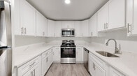 This 3-bedroom, 2-bathroom unit at Coleman Towers offers a well-appointed single-floor layout designed for comfortable living. The renovated kitchen is a standout feature, showcasing crisp white shaker-style cabinetry, quartz countertops, and a full suite of stainless steel appliances including a range, over-the-range microwave, and dishwasher. Light wood-style flooring runs throughout the unit, creating a cohesive and modern aesthetic. The spacious living area is bathed in natural light and opens to a private balcony with outdoor views, providing a seamless indoor-outdoor connection. A wide hallway connects the three well-sized bedrooms, each finished with neutral tones and continued wood-style flooring. Select bedrooms feature multiple windows that invite natural light and leafy outdoor views. The two bathrooms are cleanly finished with white vanities, mirrored medicine cabinets, brushed nickel fixtures, and tiled tub and shower surrounds. One bathroom includes a full soaking tub, while the other offers a walk-in shower. Recessed lighting and a bright, neutral color palette throughout contribute to the unit's clean, move-in-ready feel.