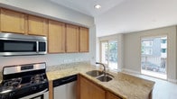 Located at 1907 Columbia in San Diego, unit #206 is a single-floor residence designed with functional living in mind. The kitchen serves as a central highlight, showcasing warm honey-toned wood cabinetry extending to the upper walls, granite countertops with golden veining, and a full suite of stainless steel appliances including a gas range, over-the-range microwave, dishwasher, and refrigerator. A double-basin sink is positioned along the peninsula, which opens toward the living area and provides a natural flow between spaces. Recessed lighting illuminates the kitchen, while a sliding glass door at the far end of the living area invites natural light and provides access to an outdoor space with views of surrounding greenery. A dedicated closet with a sliding panel door and a hanging rod offers organized storage. The in-unit laundry closet, housing a stacked washer and dryer, adds everyday convenience just off the kitchen. The bathroom is finished with matching granite countertops, light wood cabinetry, tile flooring, and a tub-shower combination enclosed by sliding glass doors. Neutral tones and clean finishes throughout create a cohesive, move-in-ready environment.