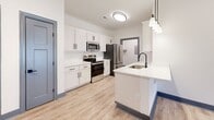 Located at 100 Hunter Hill Rd in Tarboro, NC, this well-designed one-bedroom, one-bathroom unit offers a smart and functional single-floor layout. The open-concept living, dining, and kitchen area serves as the heart of the home, finished with light wood-style luxury vinyl flooring and crisp white walls throughout. The kitchen is appointed with white shaker-style cabinetry, black hardware accents, white quartz countertops, and a full suite of stainless steel appliances including a range, microwave, dishwasher, and refrigerator. A peninsula with a single-basin sink and pendant lighting adds both workspace and a casual dining option. The bedroom is a comfortable, well-proportioned retreat featuring a ceiling fan, a large window that brings in natural light and outdoor views, and bold blue baseboard accents that add a modern touch. A dedicated closet with built-in shelving and a hanging rod provides ample storage. The bathroom includes a full soaking tub and shower combination with clean white surround. Additional highlights include a laundry area, pantry, patio access, and utility spaces, making this unit as practical as it is inviting.
