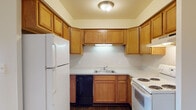 This single-floor residence in Riverview, Michigan offers a thoughtfully laid-out 1-bedroom, 1-bathroom floor plan designed for comfortable everyday living. The living area is generously sized, featuring soft wall-to-wall carpeting, recessed lighting, and a sliding glass door dressed with vertical blinds that floods the space with natural light and provides access to the outdoors. A half-wall partition visually separates the living area from the entry, adding architectural interest while maintaining an open feel. The kitchen is well-appointed with warm oak cabinetry, a tiled backsplash in a diamond pattern, and white appliances including a refrigerator, electric range, and dishwasher. Dark hardwood-style flooring grounds the kitchen and extends into the bathroom and entry areas, providing a clean contrast to the carpeted rooms. The bedroom is a quiet, comfortable retreat with plush carpeting, a large window with vertical blinds, and a six-panel door leading to the hallway. The bathroom features a long vanity with oak cabinetry and an extended countertop, a large mirror, tiled shower, and matching hardwood-style flooring, offering both practicality and style throughout this well-maintained Riverview home.