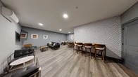 This well-appointed one-bedroom, one-bathroom residence at 21 Lakeside Ave in Pompton Lakes, NJ offers a clean, modern aesthetic throughout. Light-toned hardwood-style flooring runs continuously across the entire unit, creating a cohesive and bright atmosphere. The kitchen is a standout feature, outfitted with crisp white shaker cabinetry, a classic subway tile backsplash, dark countertops, and a full suite of stainless steel appliances including a range, microwave, dishwasher, and refrigerator. A dedicated in-unit laundry area with a stacked washer and dryer adds everyday convenience. The open layout allows the kitchen to flow naturally toward the living area, which is bathed in natural light from a large picture window overlooking the streetscape, complemented by a wall-mounted HVAC unit. The generously sized primary bedroom features recessed lighting, two closets including a walk-in, and a clean, minimalist design with ample room to furnish comfortably. The bathroom is finished with large-format gray tile surrounding a soaking tub with a handheld showerhead, white vanity cabinetry, and dark countertops. Crisp white walls and recessed lighting throughout lend the entire residence a fresh, move-in-ready appeal.