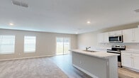 Located at 4792 White Fox Lane in Jacksonville, FL, this single-story home offers a well-designed layout with three bedrooms, three bathrooms, a garage, and dedicated laundry room. The open-concept kitchen and living area serves as the heart of the home, featuring wood-look hard flooring, white cabinetry, light stone countertops, a center island with a sink, and stainless steel appliances including a refrigerator, range, and microwave. A sliding glass door and multiple windows flood the living room with natural light and provide views of the outdoors, while plush carpeting adds warmth underfoot. Neutral warm-gray walls and a textured ceiling carry throughout, creating a cohesive and calm aesthetic. Connecting hallways lead to the three bedrooms, each finished with soft carpet. The generously sized primary bedroom includes a private en-suite bathroom with a walk-in shower and wood-look flooring, alongside a spacious walk-in closet outfitted with wire shelving. Four total closets provide ample storage throughout the home. The dedicated laundry room houses a full-size washer and dryer. The attached garage offers a concrete floor, water heater, and electrical panel, providing practical utility space to complete this functional and move-in ready home.
