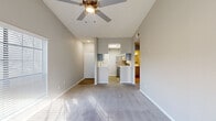 This single-floor residence offers a well-organized layout designed for comfortable everyday living. The living room serves as the focal point of the home, showcasing vaulted ceilings with a ceiling fan, soft carpet flooring, and a fireplace flanked by large windows fitted with horizontal blinds. Abundant natural light streams across the space, enhancing the open, airy feel created by the elevated ceiling line.

Adjacent to the living area, the open-concept layout provides a clear sightline into the kitchen, which features a galley-style configuration with light wood-look flooring, gray shaker cabinetry with matte black hardware, white quartz countertops, a stainless steel sink, and stainless steel appliances including a refrigerator and electric range with a dishwasher. A peninsula counter defines the transition between the kitchen and living areas.

The bedrooms are carpeted and receive natural light through sizable windows with blinds, offering a quiet and comfortable retreat. The bathroom includes a full tiled tub-shower combination, wood-look flooring, and notably, a stacked washer and dryer unit conveniently located within the space. Overall, the home presents a clean, neutral palette throughout.