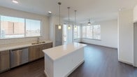 This well-designed single-floor residence offers a thoughtful layout with modern finishes throughout. The open-concept kitchen serves as the heart of the home, showcasing light wood cabinetry, white quartz countertops, a subway tile backsplash, and a full suite of stainless steel appliances including a refrigerator, range, and microwave. A large central island with pendant lighting above provides additional prep space and casual seating. Dark hardwood-style flooring runs throughout the main living and kitchen areas, adding warmth and contrast to the bright, neutral palette. The living area benefits from abundant natural light through large windows with blinds and a sliding glass door, complemented by a ceiling fan overhead. Multiple bedrooms feature plush carpeting, ceiling fans, and ample closet access, offering comfortable and versatile living spaces. The primary bathroom is fitted with a wide vanity, wood-toned cabinetry, a quartz countertop, and a large mirror with modern lighting. A secondary bathroom includes a tiled tub-shower combination, a single vanity, and a coordinating wood-finish cabinet. In-unit laundry is also present, adding everyday convenience. The overall aesthetic is clean, contemporary, and move-in ready.