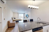 This efficiently designed 1-bedroom, 1-bathroom unit offers a thoughtful open-concept floor plan that maximizes every square foot. The kitchen serves as a functional centerpiece, featuring white shaker cabinetry, dark granite countertops, a white subway tile backsplash, and a full suite of stainless steel appliances including a gas range, microwave, French door refrigerator, and dishwasher. A granite-topped kitchen island with pendant lighting above provides additional prep space and separates the kitchen from the living area.

The open living area flows seamlessly from the kitchen, offering flexibility for both lounging and dining arrangements. Light wood-look flooring extends throughout, contributing to a clean, cohesive aesthetic. The bedroom is generously proportioned, featuring large sliding windows that invite abundant natural light and provide outdoor views of the surrounding neighborhood.

The bathroom continues the refined finishes found throughout, with a matching dark granite vanity countertop, an undermount sink with brushed nickel fixtures, and a tiled shower/tub combination with glass sliding doors. A walk-in closet with built-in shelving is conveniently accessible from the bathroom. The unit's neutral color palette and recessed lighting create a bright, modern ambiance throughout.