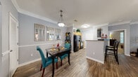 This single-floor residence offers a thoughtfully designed layout that balances functionality and comfort throughout its interconnected living spaces. The open-concept living and dining area forms the heart of the home, finished with warm wood-style flooring and crowned with elegant crown molding. The living room provides a welcoming atmosphere, featuring a ceiling fan and large windows that invite natural light. The adjacent dining area includes a stylish pendant light fixture and a chair rail detail along the walls, adding a refined architectural touch.

The galley-style kitchen is equipped with warm wood cabinetry, granite-style countertops, black appliances, and a stainless steel sink — offering an efficient and practical cooking space. A door from the kitchen provides additional access within the unit.

The primary bedroom is carpeted for comfort and features a ceiling fan, a large window overlooking greenery, and generous wall space. A second bedroom also benefits from natural light through dual windows, offering a bright and versatile room. A walk-in closet with built-in wire shelving provides ample storage.

The bathroom features a single-sink vanity with wood cabinetry, granite-style countertops, a large mirror, and wood-style flooring, completing this well-rounded and move-in-ready home.