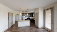 This single-story residence in Grand Prairie, Texas offers a well-designed, open-concept layout with thoughtful finishes throughout. The kitchen serves as the heart of the home, showcasing rich dark cabinetry, granite countertops, and a full suite of stainless steel appliances including a refrigerator, electric range, microwave, and dishwasher. A center island with a granite surface provides additional prep space and casual seating, while pendant lighting and a track light fixture add a modern touch. Dark hardwood-style flooring runs throughout the main living and hallway areas, complementing the neutral, light-toned walls.

The living area is bright and welcoming, with large windows dressed in blinds that frame outdoor views of the surrounding neighborhood's green landscaping. Bedrooms feature plush carpeting, ceiling fans, and windows that invite natural light. The primary bathroom is generously appointed with a dual-sink vanity topped in granite, dark cabinetry, a glass-enclosed walk-in shower with tile surround, and a separate soaking tub. An arched passageway adds an architectural detail that enhances the flow between spaces. A clean, well-lit hallway connects the rooms, completing this functional and attractively finished home.