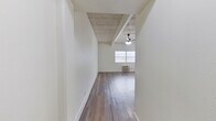 This 2-bedroom, 1-bathroom unit offers a practical and well-organized single-floor layout. Throughout the space, wood-look flooring provides a consistent and clean aesthetic, while crisp white walls contribute to a bright, open feel. A defining architectural feature is the exposed concrete beam ceiling, visible in the main living area and bedrooms, adding an industrial character to the otherwise minimalist design. The spacious primary bedroom is generously sized and includes a window for natural light and a wall-mounted air conditioning unit. The second bedroom also features a window with natural light and painted brick accent walls, adding texture to the room. The living area benefits from natural light through a large window, a ceiling fan, and a wall-mounted AC unit for climate control. The kitchen is efficiently designed with gray cabinetry, a granite-style countertop, a stainless steel sink, and an electric range. The bathroom is well-appointed with a full tub-shower combination, a white vanity with a mirrored medicine cabinet, and light wood-look tile flooring. Two hallways connect the rooms seamlessly, and a closet provides additional storage. Bold black interior doors with gold hardware add a stylish contrast throughout the unit.