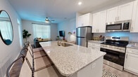 Located at Jefferson Ridge Drive in Jeffersonville, Indiana, this single-floor residence offers a thoughtfully designed layout comprising one bedroom, two bathrooms, a kitchen, living room, laundry room, and a dedicated closet. The open-concept kitchen is a standout feature, showcasing granite countertops, a large center island with an undermount sink, crisp white shaker cabinetry extending to the ceiling, and a full suite of stainless steel appliances including a refrigerator, range, and built-in microwave. Wood-look flooring runs throughout the main living areas, lending a clean, contemporary feel. The living room is bright and welcoming, with multiple windows dressed in blinds and sheer curtains, a ceiling fan, and direct access to an entry door with transom window above, allowing ample natural light. The primary bedroom features plush carpet, a generous window with drape panels, and comfortable proportions well-suited for a full furniture arrangement. The bathrooms are finished with wood-look flooring, clean neutral walls, and a tub-shower combination. A dedicated laundry room accommodates a stacked washer/dryer unit alongside the water heater, maximizing functional use of the space. Overall, the residence presents a modern, efficient, and comfortable living environment.