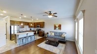 This two-story home offers a thoughtfully designed layout that blends functionality with comfortable, everyday living. The main floor showcases an open-concept floor plan where the kitchen and living area flow seamlessly together, creating a spacious and connected environment.

The kitchen is outfitted with rich, dark wood cabinetry, stainless steel appliances including a range and microwave, and light-toned countertops that provide a striking contrast. A kitchen island with bar-height seating and industrial-style metal stools serves as both a prep space and a casual dining area. Pendant lighting hangs above the island, complementing the recessed lighting throughout the ceiling for a well-lit, inviting atmosphere.

The adjacent living area features warm hardwood flooring that extends across the open space, anchored by a classic area rug. A ceiling fan with integrated lighting adds both comfort and a traditional touch. Crown molding along the ceiling lends a refined architectural detail to the room. The neutral wall tones and natural light contribute to a bright, airy ambiance throughout the main floor.

The second floor provides additional living and sleeping spaces, completing a versatile home suited for a range of lifestyles. Overall, the space balances classic design elements with modern finishes.