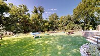 This expansive outdoor amenity area offers a diverse range of recreational and social spaces, all thoughtfully integrated within a lushly landscaped setting. Manicured synthetic turf stretches across the grounds, providing a clean, evergreen foundation for multiple activity zones. A standout feature is the multi-hole putting green, complete with sand bunkers, natural boulder accents, and low-profile landscape lighting along its borders — creating an engaging golf experience surrounded by mature trees and native plantings.

Adjacent to the putting green, a dedicated lawn games area accommodates ping-pong and cornhole, with Adirondack-style seating positioned nearby for spectators and those relaxing in the sun. The grounds are bordered by dense, layered landscaping featuring ornamental grasses, flowering shrubs, and towering trees that provide both shade and a sense of natural seclusion.

A raised stone-paver patio serves as a social hub, featuring tiered retaining walls, a built-in grill station, and covered outdoor dining beneath shade sails. Steps lead down from the patio to the lawn level, creating a natural transition between spaces. Pathway lighting throughout ensures usability into the evening hours. The overall design balances active recreation with relaxed outdoor living in a well-appointed, resort-style environment.