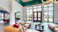 Located at 7222 S Peek Rd in Houston, TX, this striking single-floor space offers a generously sized, open-plan interior that makes a bold architectural statement from the moment you enter. Soaring double-height ceilings define the main lounge area, which is anchored by floor-to-ceiling black-framed windows that invite abundant natural light and offer clear views of the surrounding greenery outside.

The design palette is sophisticated and contemporary, pairing crisp white walls with rich teal accent walls and ceiling details that add depth and visual drama throughout. Large-format dark tile flooring runs throughout much of the space, complemented by distinctive patterned tile inlays — including a geometric diamond motif and a classic herringbone layout — that serve as eye-catching design focal points.

Furnishings are carefully curated, featuring a tan leather sectional sofa with colorful throw pillows, plush cream boucle accent chairs with gold-toned bases, and deep burgundy velvet seating arrangements. Curated artwork adorns the walls, adding a gallery-like quality to the lounge and seating alcoves.

A dedicated reception or leasing area is framed by elegant black-framed glass partition doors and decorative patterned wallcovering, creating a defined yet open professional zone. Throughout, the space balances a welcoming, residential warmth with the polished finish of a high-end commercial environment.