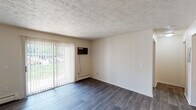 Located on N Drake Rd in Kalamazoo, Michigan, this single-floor unit offers a practical and well-organized layout designed for comfortable everyday living. The living area is a welcoming, open space finished with durable wood-style flooring and a textured ceiling. Large sliding glass doors fitted with vertical blinds flood the room with natural light and provide views of the surrounding greenery, while a baseboard heating system runs along the perimeter walls. An in-wall air conditioning unit offers year-round climate control. The kitchen is efficiently designed with dark espresso cabinetry, light stone-finish countertops, and stainless steel appliances, including a full-size refrigerator. A pass-through counter connects the kitchen to the adjacent area, which features additional storage with built-in shelving and a closet. The bedroom is carpeted for comfort, with a large window that brings in natural light and offers pleasant outdoor views, complemented by its own baseboard heater. The bathroom is clean and functional, featuring a full tub and shower combination with classic white subway tile accented by a subtle blue tile border. Wood-style flooring extends into the bathroom, tying the space together cohesively throughout.