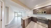 This well-appointed one-bedroom, one-bathroom unit at 4805 W Genesee St in Syracuse, New York offers a thoughtfully designed layout with contemporary finishes throughout. The open-concept kitchen and living area serves as the heart of the unit, where rich dark-brown shaker cabinetry, striking granite countertops with herringbone tile backsplash, and a full suite of stainless steel appliances — including a range, microwave, and refrigerator — create a polished, functional kitchen. A large granite-topped island with an undermount sink adds both workspace and casual dining potential. Light hardwood-style flooring flows seamlessly throughout the entire unit, enhancing the bright, airy atmosphere. The living area is generously sized, highlighted by a statement multi-blade ceiling fan and a door leading to a private balcony, where large windows invite abundant natural light and outdoor views. The spacious primary bedroom features a wide window with outdoor views, neutral toned walls, and easy access to a dedicated closet. The bathroom is elegantly finished with a granite vanity countertop, an undermount sink with brushed nickel fixtures, and a marble-tiled shower surround. Clean lines, neutral tones, and modern hardware tie the entire space together cohesively.