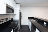 Located at 8440 Fountain Ave in the heart of West Hollywood, CA, this single-floor unit offers a clean, contemporary aesthetic with a thoughtfully designed open layout. Dark hardwood-style flooring runs throughout the space, providing a striking contrast against the crisp white walls and trim.

The open-concept kitchen is a standout feature, anchored by a generous island with sleek black countertops, a double stainless steel sink, white cabinetry, and stainless steel appliances including a refrigerator and range. The kitchen flows seamlessly into the living area, which is bright and open with recessed lighting and access to natural light through sliding windows.

The living areas are spacious and versatile, with large windows that allow natural light to fill the rooms while offering views of the exterior. One room features a ceiling fan with integrated lighting, adding both comfort and style. Recessed lighting throughout ensures well-lit interiors at all times of day.

The bathroom is finished in a clean, neutral palette with a full tub-shower combination, chrome fixtures, and a grab bar. Additional rooms provide flexible spaces suitable for bedrooms or offices, each with ample wall space and dark flooring. The unit's minimalist design and modern finishes make it a well-appointed space in a prime West Hollywood location.