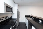 Located at 8440 Fountain Ave in the heart of West Hollywood, CA, this single-floor unit offers a clean, contemporary aesthetic with a thoughtfully designed open layout. Dark hardwood-style flooring runs throughout the space, providing a striking contrast against the crisp white walls and trim.

The open-concept kitchen is a standout feature, anchored by a generous island with sleek black countertops, a double stainless steel sink, white cabinetry, and stainless steel appliances including a refrigerator and range. The kitchen flows seamlessly into the living area, which is bright and open with recessed lighting and access to natural light through sliding windows.

The living areas are spacious and versatile, with large windows that allow natural light to fill the rooms while offering views of the exterior. One room features a ceiling fan with integrated lighting, adding both comfort and style. Recessed lighting throughout ensures well-lit interiors at all times of day.

The bathroom is finished in a clean, neutral palette with a full tub-shower combination, chrome fixtures, and a grab bar. Additional rooms provide flexible spaces suitable for bedrooms or offices, each with ample wall space and dark flooring. The unit's minimalist design and modern finishes make it a well-appointed space in a prime West Hollywood location.