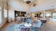 Located at 2620 W Sunshine St in Springfield, Missouri, this single-floor community clubhouse offers a generously expansive layout designed for both socializing and relaxation. The space is defined by its contemporary design, featuring soaring double-height ceilings in the main lounge area, dramatic sputnik-style chandeliers, and an abundance of natural light streaming through large windows and glass entry doors.

The first living area serves as the central gathering hub, anchored by a sleek, tiled fireplace that rises to the ceiling and is flanked by lush indoor plants. Eclectic, colorful seating arrangements — including patterned accent chairs and modern swivel seats — are arranged across patterned area rugs atop light hardwood-style flooring. Adjacent to this lounge is a full kitchen bar with bar-height seating, stainless steel appliances, and a striking textured tile backsplash.

The second living area transitions into a more casual, multi-use space with high ceilings accented by teal acoustic panels and large windows overlooking an outdoor pool area. High-top communal tables with upholstered seating line one wall, decorated with a sculptural acoustic tile feature wall and mounted displays.

A connecting hallway, adorned with vibrant artwork and decorative glass-panel dividers, leads to a game room complete with a billiard table, adding a recreational dimension to the overall space.