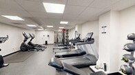 Located at 2920 5th Ave in Troy, New York, this fitness center offers a well-organized, single-floor exercise space designed to accommodate a full range of workout routines. The room features a drop-panel ceiling outfitted with recessed fluorescent lighting panels that provide bright, even illumination throughout. The flooring consists of durable speckled rubber, ideal for high-traffic gym use and equipment placement.

The cardio section is equipped with multiple treadmills from Spirit and Endurance brands, along with elliptical trainers from Sole and a stationary upright bike, providing ample options for cardiovascular workouts. Rowing machines are also present, adding variety to the cardio offerings. The strength training area features a multi-station cable machine system and a squat/power rack with free weights, supporting a comprehensive resistance training regimen. A TKO adjustable workout bench is available for free weight exercises.

A dedicated area in the rear of the space includes a wood-toned flooring section near the cable station, adding a slight design contrast to the otherwise uniform gray floor. A restroom is accessible directly within the space for user convenience. The clean, white walls and structured layout create a functional and focused environment, making this fitness center a practical and fully equipped facility for daily exercise.