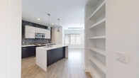 Located at 11560 Old Georgetown Rd in North Bethesda, Maryland, this single-floor space showcases a clean, contemporary design with an open-concept layout and high-quality finishes throughout. Light wood-tone flooring flows seamlessly across the living and kitchen areas, creating a cohesive, airy atmosphere.

The kitchen is a standout feature, centered around a sleek island with a white quartz countertop, an undermount sink, and a dark charcoal base. Stainless steel appliances — including a gas range, over-the-range microwave, and refrigerator — are complemented by two-toned cabinetry: high-gloss white upper cabinets and dark lower cabinets. A distinctive penny-tile mosaic backsplash in deep blue-gray tones adds texture and visual interest. Industrial-style pendant lights hang above the island, enhancing the modern aesthetic.

Adjacent to the kitchen, a built-in shelving unit provides generous display and storage space, while a large window floods the living area with natural light. A separate room offers a bright, minimalist retreat with neutral walls and light flooring.

The bathroom features large-format gray tile flooring, a white vanity with a dark countertop, and a backlit mirror, delivering a sleek, spa-inspired finish.