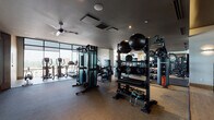 This well-appointed fitness center in Denver's Cherry Creek neighborhood offers a comprehensive workout environment designed with both functionality and aesthetics in mind. The space features a sophisticated dark ceiling with recessed lighting and ceiling fans, contrasted by warm wood-paneled accent walls that lend a refined, contemporary character throughout.

The cardio zone takes full advantage of floor-to-ceiling windows, providing panoramic views of the surrounding Denver skyline while using ellipticals, treadmills, and stair climbers. Natural light floods this area, creating an energizing atmosphere for cardio training.

The strength training area is extensively equipped with a multi-station cable machine, a full rack of Matrix and Torque brand equipment, adjustable benches, and a large selection of dumbbells organized on tiered racks. Medicine balls, kettlebells, and resistance accessories are neatly stored for functional training needs.

A dedicated free weights and functional training zone features rubber flooring for safety and durability, a large-format wall-mounted display screen, and expansive floor-to-ceiling mirrors that visually enlarge the space. The entry area showcases warm hardwood flooring and framed glass double doors, providing a polished transition into the facility. Overall, the space delivers a premium, hotel-caliber fitness experience.