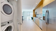 This thoughtfully designed one-bedroom unit offers a compact yet efficient single-floor layout that maximizes every square foot. The open-concept interior is anchored by a sleek, fully equipped kitchen featuring flat-front light wood cabinetry, white quartz countertops, a marble-style tile backsplash, and a full suite of stainless steel Bosch appliances, including a gas cooktop, wall oven, over-range microwave, dishwasher, and refrigerator. Light hardwood flooring runs throughout, lending warmth and visual continuity across the space. The living area is bathed in natural light through floor-to-ceiling windows and a sliding glass door, offering outdoor views and a bright, airy ambiance. Clean white walls and a neutral palette keep the space feeling open and contemporary. The bedroom is generously sized with large windows that frame outdoor views, a dedicated walk-in closet, and direct access to the main living corridor. The bathroom is finished with large-format neutral tiles, a glass-enclosed soaking tub with overhead shower, and a wood-accented vanity. Together, these elements create a cohesive, modern living environment that balances style and functionality.
