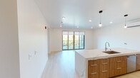 Unit 613 at 1431 Q St in Sacramento's Midtown neighborhood is a contemporary single-floor apartment showcasing clean, modern design throughout. The open-concept living and kitchen area is anchored by a large quartz waterfall island with an undermount stainless steel sink and pendant lighting overhead. The kitchen is fully equipped with flat-front wood-toned cabinetry, a gas range with stainless steel appliances, a matching refrigerator, and a sleek marble-style backsplash. Light wood-style flooring flows throughout the main living areas, complementing the bright white walls and recessed lighting. Sliding glass doors lead from the living area to a private balcony, filling the space with natural light and offering treetop and city views. The bedrooms are well-sized, featuring large windows with views of the surrounding neighborhood. The primary bedroom includes a ceiling fan and a stylish sliding barn door leading to a walk-in closet. The bathrooms are elegantly finished with large-format marble-look tile, vessel sinks, wood-toned vanities, LED-backlit mirrors, and a soaking tub. A secondary bathroom features a similar refined aesthetic with a vessel sink and marble tile surround, providing a cohesive, upscale feel throughout the unit.