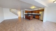 This two-story home offers a well-organized layout across two floors, with the main living areas on the ground floor and bedrooms distributed between both levels. The open-concept ground floor seamlessly connects the living room and kitchen, creating a spacious, communal area ideal for everyday living. Large tile flooring runs throughout the main level, complementing the bright, airy atmosphere enhanced by a wide front window that invites natural light. The front entry features a bold dark door framed by a large window with views of surrounding greenery.

The kitchen is a standout feature, showcasing rich wood cabinetry, dark granite countertops, stainless steel appliances including a refrigerator with ice dispenser and a microwave, and a central island that provides additional prep and storage space. A dedicated laundry room continues the design consistency with matching wood cabinetry, granite countertops, and tile flooring.

The bedrooms are carpeted and each include ceiling fans, offering a comfortable and quiet retreat. The primary bedroom is generously proportioned with closet access. All three bathrooms are finished with tile flooring, wood vanities, and dark granite countertops, with at least one full bath featuring a tiled tub-shower combination.