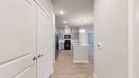 This thoughtfully designed 2-bedroom, 2-bathroom residence offers a functional and modern single-floor layout. The open-concept kitchen serves as the heart of the home, featuring gray shaker-style cabinetry extending to the ceiling, granite countertops, a white subway tile backsplash, and stainless steel refrigerator alongside black appliances. A central kitchen island with a granite top and undermount sink provides additional prep space and casual seating potential, illuminated by a stylish pendant light overhead. Light wood-look flooring flows throughout the main living areas, enhancing the bright, clean aesthetic. The living room benefits from natural light through large windows and includes access to an exterior door, offering outdoor connectivity. Both bedrooms are carpeted for comfort, with the primary bedroom featuring a ceiling fan and windows that allow in natural light. The primary suite includes a well-appointed bathroom with a granite-topped dual vanity, gray cabinetry, and direct access to a walk-in closet with wire shelving. The second bathroom mirrors the same refined finishes. A hallway connects the spaces seamlessly, and two closets provide ample storage. The overall palette of soft grays, whites, and warm wood tones creates a cohesive, contemporary ambiance throughout.