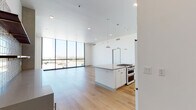 This contemporary high-rise residence offers a striking open-concept layout defined by clean lines, light wood flooring, and an abundance of natural light. Floor-to-ceiling windows span multiple rooms, framing sweeping panoramic views of the surrounding cityscape and distant mountain ranges, creating a seamless connection between the interior and the outdoors.

The kitchen is a central highlight, featuring a large island with a quartz countertop, a professional-grade gas range, stainless steel appliances including a built-in microwave and full-size refrigerator, and a herringbone-patterned tile backsplash. White shaker cabinetry extends to the ceiling, maximizing storage, while pendant lighting adds a refined touch. A beverage refrigerator and open shelving with decorative tile accents further enhance the space.

The living areas are generously proportioned, bathed in natural light through expansive glass walls, with warm wood flooring flowing throughout. Bedrooms continue the theme of abundant light and views, each with large floor-to-ceiling windows overlooking the city and mountains.

The bathrooms are finished with large-format tile, white cabinetry, quartz countertops, and gold hardware accents. The primary bath includes a glass-enclosed walk-in shower, while a secondary bath offers a tiled soaking tub and shower combination. Recessed lighting and illuminated mirrors complete the refined aesthetic throughout.