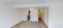 This two-story residence offers 2 bedrooms and 1.5 bathrooms across a thoughtfully arranged floor plan. The main level features a spacious living area with neutral wall-to-wall carpeting that creates a warm and inviting atmosphere. Flush-mounted ceiling lighting provides consistent illumination throughout. Adjacent to the living space, the kitchen is equipped with dark cabinetry, white appliances, and tile flooring, offering a practical workspace for everyday cooking. A dedicated entryway with a staircase connects the two floors, with a closet conveniently located near the entry. The clean white walls and simple architectural lines throughout the main level contribute to a bright, open feel. The two-floor layout allows for a natural separation between the living and sleeping areas, providing added privacy. The half bathroom on one level and full bathroom on the other ensure convenience for both residents and guests. Overall, the space presents a straightforward and efficient design, well-suited for comfortable everyday living.