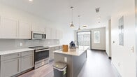 Located on Belcourt Avenue in the heart of Nashville, TN, this thoughtfully designed one-bedroom, one-bathroom residence offers a modern open-concept layout with clean lines and contemporary finishes throughout. The kitchen serves as the focal point of the living space, showcasing a central island with a double-basin sink, crisp white quartz countertops, two-tone cabinetry in white and gray, a classic subway tile backsplash, and stainless steel appliances including a refrigerator, range, microwave, and dishwasher. Stylish pendant lights hang above the island, adding a refined touch to the space. Rich hardwood-style flooring flows seamlessly from the kitchen into the open living area, which is filled with natural light through a large sliding glass door fitted with vertical blinds, offering views of the outdoors. The bedroom provides a comfortable and private retreat, complemented by two closets for ample storage. The bathroom features gray cabinetry with a white countertop vanity and light tile flooring, maintaining the home's cohesive modern aesthetic. A utility room and additional storage complete the practical layout. The overall ambiance is bright, clean, and contemporary, ideal for those seeking a stylish urban residence in one of Nashville's most sought-after neighborhoods.