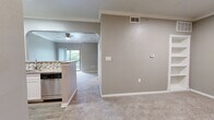 This single-floor, one-bedroom unit offers a thoughtfully designed layout that maximizes functionality across its compact footprint. The living area features plush carpeting, crown molding, and a ceiling fan, creating a comfortable and cohesive space. An arched passageway connects the living area to the kitchen, which is equipped with stainless steel appliances including a range, over-the-range microwave, and dishwasher. The kitchen also boasts white cabinetry, granite countertops, a mosaic tile backsplash, and hardwood-style flooring, giving it a polished, modern aesthetic. Natural light filters in through a sliding glass door that leads to an outdoor area, adding brightness to the open living and kitchen space. The bedroom is a generously sized retreat with plush carpeting, a ceiling fan, and a window with natural light. A standout feature is the built-in shelving unit nestled into one corner, providing practical storage and display space. The bedroom also connects to a private bathroom with wood-style flooring and a vanity with ample cabinet space. A dedicated laundry area houses a stacked washer and dryer unit alongside wire shelving for additional storage. Throughout the unit, neutral gray tones and white trim create a clean, modern atmosphere.