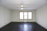 This single-floor space offers a functional and straightforward layout with a blend of classic and updated elements. The main living area is generously proportioned, showcasing rich, dark hardwood flooring that extends throughout. Multiple windows allow natural light to filter in, brightening the neutral-toned walls, while a ceiling fan with an integrated light fixture provides both comfort and overhead illumination. A wall-mounted air conditioning unit adds practical climate control.

The kitchen is tucked into a compact galley-style corridor, outfitted with grey cabinetry, dark countertops, a gas range, and a full-size black refrigerator. Recessed lighting and dark hardwood-style flooring keep the kitchen cohesive with the rest of the unit.

The bathroom is accessed through a classic multi-panel door and features light tile flooring, a white vanity with mirror, and a shower/tub combination. The textured walls add a subtle detail to the otherwise clean and minimal design.

Overall, the space maintains a practical ambiance, combining timeless hardwood flooring and classic architectural details with select modern updates in the kitchen and bathroom areas.