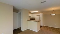 Located at 2945 Layfair Dr. in Flowood, Mississippi, this single-floor unit offers a practical and well-organized layout designed for comfortable everyday living. The open-concept design connects the kitchen and living area seamlessly, creating a cohesive and functional space throughout.

The kitchen is a standout feature, equipped with crisp white cabinetry that provides generous storage space both above and below. A peninsula with a dark granite-style countertop extends into the living area, offering additional prep space and serving as a natural divider between the kitchen and the main living zone. A white refrigerator and built-in cooktop complete the kitchen's functional setup, while a ventilation hood is mounted above the cooking surface.

The living area is finished with wall-to-wall carpeting in a warm, neutral tone that adds a sense of comfort underfoot. The walls are painted in a soft beige, contributing to an overall warm and inviting ambiance. A textured ceiling runs throughout, and overhead lighting ensures the space remains bright and well-illuminated.

A closet with sliding doors is visible adjacent to the main living space, offering convenient storage. The layout flows efficiently, making the most of the available square footage in this straightforward, single-level home.