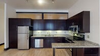 Located at 300 N Main St in downtown Winston-Salem, NC, this single-floor unit offers a thoughtfully designed layout with modern finishes throughout. The kitchen is a standout feature, showcasing rich dark espresso cabinetry that extends to the ceiling with upper glass-paneled accent cabinets, granite countertops, a full suite of stainless steel appliances including a refrigerator, dishwasher, microwave, and electric range, and a kitchen island for additional prep and seating space. Light hardwood flooring flows consistently throughout the unit, providing a warm contrast to the bold dark trim and door frames that define the interior aesthetic. The living and bedroom areas are open and versatile, featuring neutral walls, track lighting, and transom-style interior windows that allow light to pass between spaces. The bathrooms offer distinct character — one features a striking glass vessel sink atop a dark vanity with a framed mirror, while the second includes a full tub and shower combination with tile flooring. The unit's clean, contemporary design, consistent material palette, and urban location make it a well-appointed space suited for modern living in the heart of Winston-Salem.