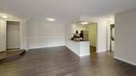 This single-floor residence offers a clean, neutral aesthetic throughout, with a thoughtful layout that balances open communal spaces and private living areas. The living area is spacious and bright, featuring dark hardwood-style flooring and a large sliding glass door fitted with vertical blinds that allows generous natural light to fill the room while providing access to outdoor views. Adjacent to the living area, the kitchen is accessible via a peninsula-style breakfast bar with dark granite countertops. The kitchen is well-equipped with white shaker cabinetry, matching dark granite surfaces, and a full suite of stainless steel appliances including a range, over-the-range microwave, dishwasher, and refrigerator. The bedrooms are carpeted in a warm, neutral tone and each features windows with horizontal blinds that invite natural light. The primary bedroom includes direct access to two separate rooms — a dedicated toilet room and a vanity area — offering a functional en-suite configuration. A second full bathroom serves the rest of the residence and features a tub-shower combination, chrome fixtures, and neutral grey walls. Throughout the space, white trim, soft grey-beige walls, and consistent finishes create a cohesive and welcoming environment.