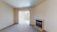 This single-floor residence offers a thoughtfully designed layout that balances open-concept living with well-defined private spaces. The living room is a standout area, featuring vaulted ceilings that create a sense of spaciousness, plush carpeting, and a tile-surround fireplace that serves as a focal point. A sliding glass door with vertical blinds opens to a balcony, filling the space with natural light and outdoor views. Adjacent to the living room, the kitchen is outfitted with white cabinetry accented by wood trim, white appliances including a refrigerator and range, tile flooring, and a peninsula breakfast bar that connects to the dining area — ideal for casual meals or entertaining. The space includes two carpeted bedrooms, each receiving natural light through window blinds. One bedroom features two mirrored sliding-door closets, while the other includes a single mirrored closet. Two full bathrooms serve the residence: one with a soaking tub and shower combination and tile flooring, and a second featuring a corner glass-enclosed shower stall, a single vanity, and matching tile flooring. The entry foyer provides a welcoming transition into the home, with tile flooring and direct sightlines into the open living and kitchen areas.