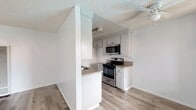 Located at 3500 Cedar Ave, Unit 210 in Long Beach, CA, this one-bedroom, one-bathroom residence offers a well-organized and efficient layout across a single floor. Light-toned hardwood-style flooring runs throughout the unit, lending a clean and cohesive look to every room.

The galley-style kitchen is thoughtfully designed, featuring white cabinetry on both sides, granite-look countertops, a stainless steel gas range with microwave above, and a double-basin sink. Abundant upper and lower cabinet storage maximizes functionality in the compact space. The kitchen opens toward the living area via a partial partition wall, creating a semi-open feel.

The bedroom is generously sized for the overall footprint of the unit, offering a sliding closet, a window that admits natural light, and a textured ceiling. A vanity with granite-look countertop and white cabinetry is accessible from within the bedroom area, bridging the space to the bathroom.

The bathroom is neatly appointed with a tub-shower combination featuring full-height gray tile surround, a window above for ventilation and light, wood-style flooring, and a clean white toilet. Throughout the unit, white walls and neutral finishes create a bright, move-in-ready atmosphere well-suited for single-occupant living in Long Beach.