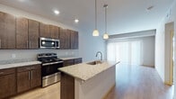 Located at 7944 Watts Rd in Madison, Wisconsin, this single-floor residence offers a thoughtfully designed open-concept layout that seamlessly connects the kitchen and living areas. The kitchen serves as the centerpiece of the space, showcasing rich dark-espresso cabinetry with sleek hardware, granite countertops, and a full suite of stainless steel appliances including a range, microwave, and refrigerator. A central island with an integrated sink and pendant lighting overhead adds both functionality and visual appeal. Light-toned hardwood flooring runs throughout the main living area, enhancing the sense of openness and warmth. Large windows with vertical and horizontal blinds allow for generous natural light while offering privacy. The bedroom is a calm, neutral retreat featuring plush carpeting, vaulted ceiling detail, and a broad window that fills the room with daylight. The bathroom is finished with dark cabinetry paired with a crisp white countertop, a full tub-shower combination, and tile flooring. A ceiling fan is also present in the unit, contributing to comfort throughout the seasons. The overall design reflects a clean, contemporary aesthetic with consistent finishes and a practical, well-organized floor plan.