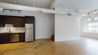 This two-floor urban loft blends industrial character with modern convenience throughout its open, airy layout. The main level is defined by polished concrete floors that extend seamlessly across the living and kitchen areas, creating a cohesive and low-maintenance foundation. Soaring ceilings with prominently exposed white ductwork lend the space a distinctive industrial aesthetic, while generous ceiling height amplifies the sense of openness and volume.

The kitchen is equipped with dark cabinetry, a stainless steel refrigerator, and a classic subway tile backsplash, offering a clean contrast against the light walls. A staircase leads to the second floor, adding a sense of verticality and functional separation between living areas. One room on the main level features a large multi-pane window that draws in natural light, complemented by a track lighting system ideal for highlighting artwork or providing flexible illumination.

A full bathroom is finished in crisp white tile with a tub-shower combination and dark wood vanity. A dedicated laundry area houses a stacked washer and dryer alongside built-in shelving and a hanging rod, providing practical storage solutions. The overall palette of white walls, concrete floors, and dark accents creates a clean, contemporary industrial ambiance throughout the space.