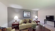 This single-floor residence offers a thoughtfully designed layout that balances comfort and functionality across its key living areas. The living room serves as the heart of the home, featuring neutral-toned walls with a warm gray accent wall, plush wall-to-wall carpeting, and ample space for multiple seating arrangements. Framed artwork adorns the walls, contributing to a calm and welcoming ambiance throughout.

The kitchen is bright and practical, finished with white cabinetry, light tile flooring, and a clean countertop workspace. A skylight adds natural light from above, while a sliding glass door opens directly onto a private outdoor balcony — ideal for enjoying fresh air and exterior views. A dedicated dining area adjacent to the kitchen provides a comfortable space for meals.

The bedroom is generously proportioned, offering soft carpeting, large windows that invite natural light, and a closet for ample storage. The room's neutral palette and understated design create a restful retreat.

The full bathroom is clean and efficiently laid out, featuring a tub-shower combination with white tile surround, a vanity with sink, and tile flooring. Throughout the residence, the consistent use of neutral tones and practical finishes creates a cohesive and livable environment.