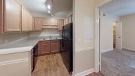 Located at 1175 Mathis Ferry Rd in Mount Pleasant, South Carolina, this single-floor unit offers a practical and comfortable layout suited for everyday living. The kitchen is well-appointed with warm wood-toned cabinetry extending to the ceiling for ample storage, light stone-look countertops, a double-basin sink, and black appliances including a full-size refrigerator and dishwasher. Track lighting overhead ensures the space is well-lit, while durable wood-look flooring adds a clean, classic finish. A peninsula-style counter provides a natural division between the kitchen and the adjacent living area, which features plush neutral carpeting and a large window fitted with vertical blinds that allow for natural light and privacy control. Crown molding accents the living area, adding a refined architectural detail. The bedroom is generously proportioned with soft carpeting, a ceiling fan with integrated lighting, and ample wall space. The bathroom includes a full tub and shower combo with white tile surround, a single vanity with a wide mirror, and chrome fixtures. This well-maintained unit combines functional design with comfortable living in a desirable Mount Pleasant location.
