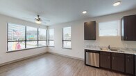 This single-floor unit presents a clean, contemporary design with a cohesive neutral color palette and light wood-look flooring throughout the main living areas. The open-concept layout connects the kitchen and living space seamlessly, creating an airy, functional environment. The kitchen is well-appointed with dark espresso cabinetry, light granite-style countertops, and a full suite of stainless steel appliances, including a refrigerator, electric range with microwave, and dishwasher. Multiple windows allow natural light to fill the space, with views of the surrounding urban environment.

The living area features recessed lighting and a ceiling fan, lending a bright and comfortable atmosphere. The bedrooms are finished with plush carpeting, ceiling fans, and windows that bring in additional natural light and outdoor views. The primary bathroom includes a dark-cabineted vanity with matching countertops, a walk-in closet, and a separate shower area. The secondary bathroom offers a full tub-shower combination, a single vanity, and wood-look flooring. Throughout, the unit maintains a consistent modern aesthetic with clean lines, recessed lighting, and neutral tones.