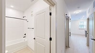 Located at 19 Harnett St in Wilmington, NC, this efficiently designed one-bedroom, one-bathroom unit offers a thoughtful layout across a single floor. The open-concept kitchen is a standout feature, outfitted with crisp white shaker cabinetry, light quartz countertops, a herringbone tile backsplash, and a full suite of stainless steel appliances including a refrigerator, range, microwave, and dishwasher. Light hardwood-style flooring runs throughout the kitchen and main living area, complementing the clean, bright aesthetic enhanced by recessed lighting. A sliding barn door adds a modern design touch to the hallway, connecting the living space to the private quarters. The generously proportioned bedroom features plush carpeting, a ceiling fan, and a row of interior transom windows that allow natural light to filter through from the adjacent living area. A sliding closet door opens to a well-organized reach-in closet with wire shelving. The bathroom is finished with matte black fixtures and hardware, a two-panel white door, and a soaking tub with a crisp white herringbone tile surround, offering a clean and polished aesthetic throughout. The overall design is modern, neutral, and move-in ready.