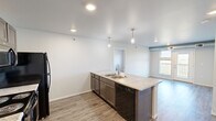This single-floor, 2-bedroom, 2-bathroom unit in Union, Box Elder, South Dakota, offers a thoughtfully designed layout with modern finishes throughout. The open-concept kitchen serves as the centerpiece of the living area, anchored by a large island with a granite-style countertop, double sink, and pendant lighting. Dark espresso cabinetry pairs with black appliances, including a range, microwave, and refrigerator, while wood-look plank flooring extends throughout the main living area, adding warmth and continuity.

The living area flows naturally from the kitchen, with a window providing views of the surrounding South Dakota landscape. Both bedrooms feature plush carpeting and windows that frame scenic rural vistas. The spacious primary bedroom includes a walk-in closet, while the second bedroom offers a standard closet with built-in shelving.

Each bathroom is finished with granite-style countertops, dark cabinetry, tile flooring, and a tub-shower combination. An in-unit laundry area is also present. The unit features a neutral color palette, recessed lighting, and a clean, contemporary aesthetic suited to comfortable everyday living.