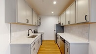 Located on the 11th floor at 933 McGee Street in Kansas City, Missouri, this efficiently designed unit offers a thoughtful layout across a single floor, comprising a living room, kitchen, and full bathroom. Throughout the space, warm-toned light wood flooring and crisp white walls create a clean, contemporary aesthetic.

The living area is bright and open, benefiting from large black-framed windows that frame elevated views of the Kansas City skyline, filling the room with natural light. Recessed ceiling lighting provides additional illumination throughout.

The galley-style kitchen is well-appointed with gray shaker-style cabinetry featuring matte black hardware, white quartz countertops, a subway tile backsplash, and stainless steel appliances including a refrigerator, dishwasher, and microwave. A wooden floating shelf adds a functional design accent.

The bathroom continues the modern design language with white cabinetry, black hardware, a white quartz vanity top, and a tiled walk-in shower enclosed by a sleek black-framed glass sliding door. The light wood flooring extends into the bathroom, maintaining visual consistency throughout the unit.

Overall, the space presents a modern, minimalist character with cohesive finishes and practical functionality.